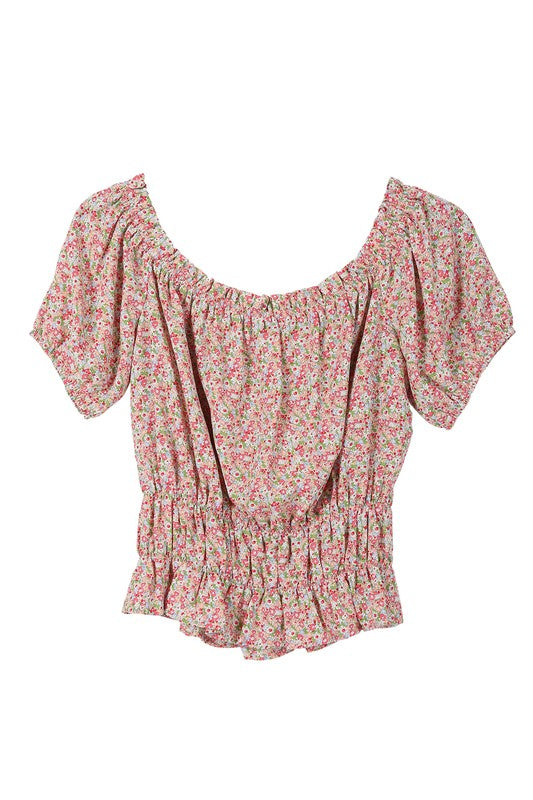 A woman wears the SL off shoulder tube top, featuring a floral print and a shirred design. The ensemble is completed with puffed sleeves and a ruffled skirt for an elegant and charming look.