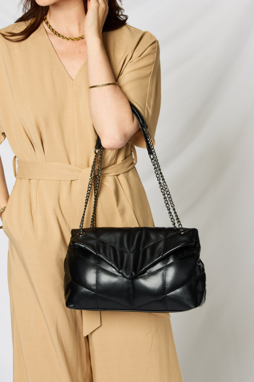 A person holding a stylish SHOMICO PU Leather Chain Handbag over their shoulder against a white background. They are dressed in a beige outfit and looking at the camera, embodying sustainable fashion.