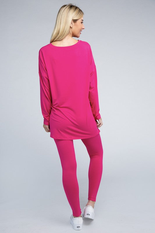 Clad in the Brushed DTY Microfiber Loungewear Set, a person stands against a plain background, showcasing its buttery soft, bright pink long-sleeve top and matching leggings, complemented by white sneakers.