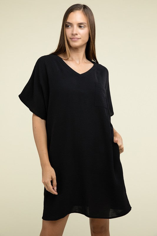 A woman wearing a loose light brown Woven Airflow V Neck T-Shirt Dress with Pockets stands against a plain background. Made from breathable fabric, this summer dress includes pockets where her hands rest as she smiles slightly.