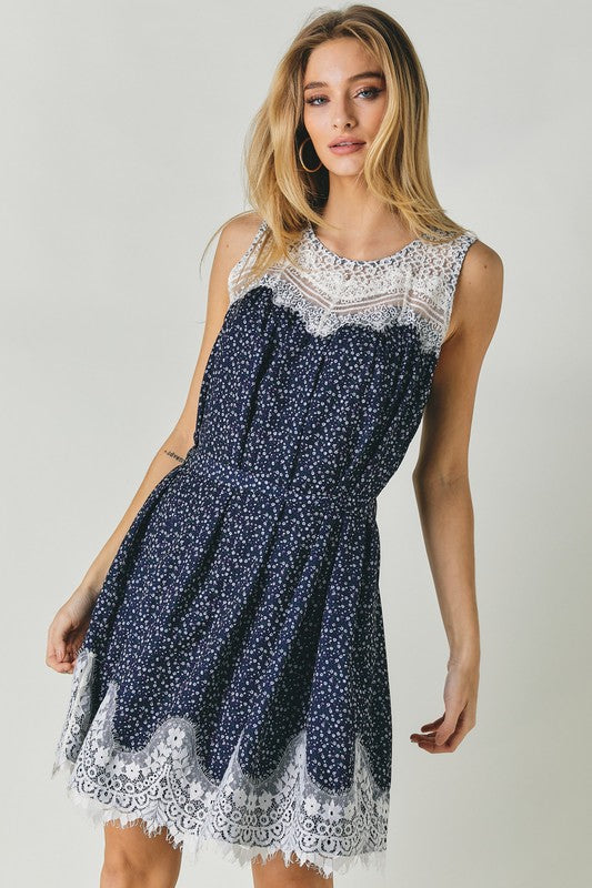 A woman wearing the Printed Sleeveless Lace Trim Mini Dress is seated against a light background.