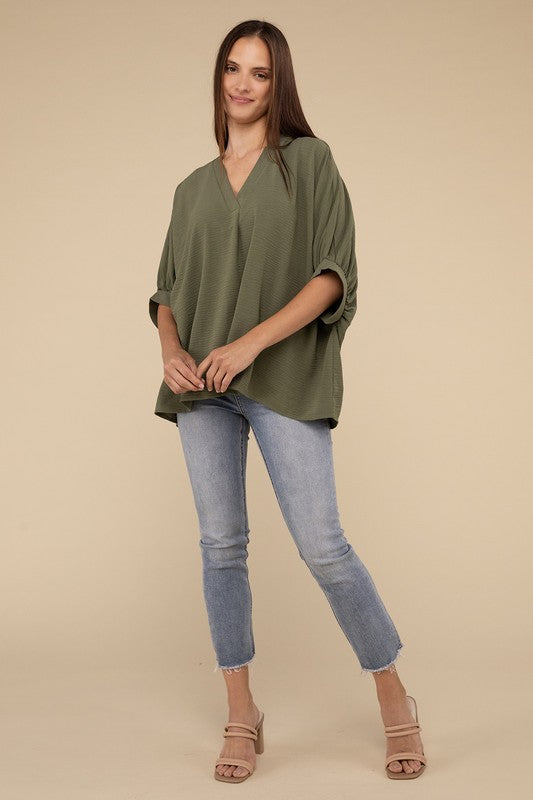A woman in a Woven Airflow V-Neck Puff half sleeve top and blue jeans stands with her hand on her hip, looking to her right.