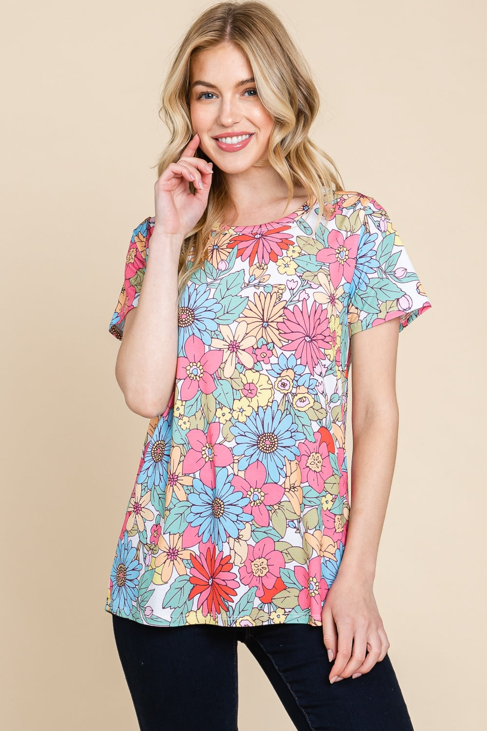 A woman wearing a vibrant BOMBOM Floral Short Sleeve T-Shirt and dark pants, posing against a beige background.