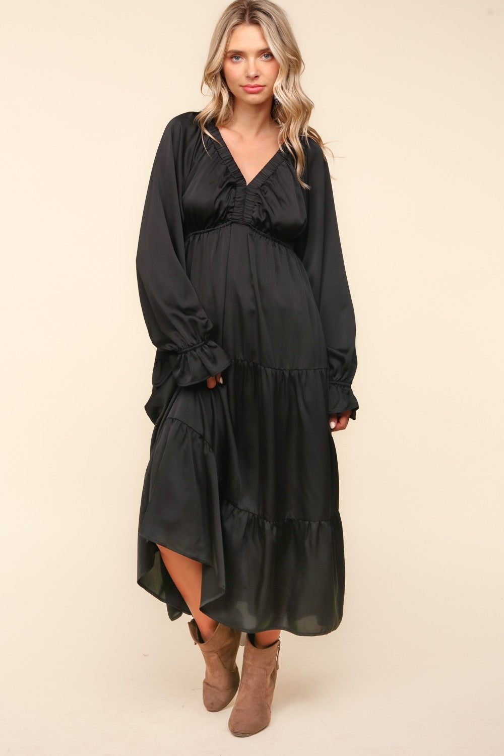 A woman stands wearing the Haptics Flounce Sleeve Tiered Midi Dress with Pockets in black, paired with brown ankle boots, against a plain background.