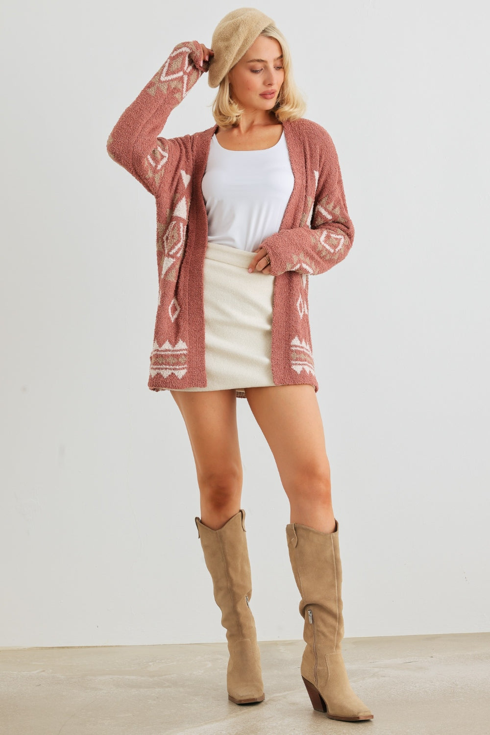 A woman wearing the VERY J/Loveriche Open Front Long Sleeve Cardigan in light pink—an absolute versatile wardrobe essential—paired with a white tank top, white skirt, and beige beret poses gracefully against a plain background.