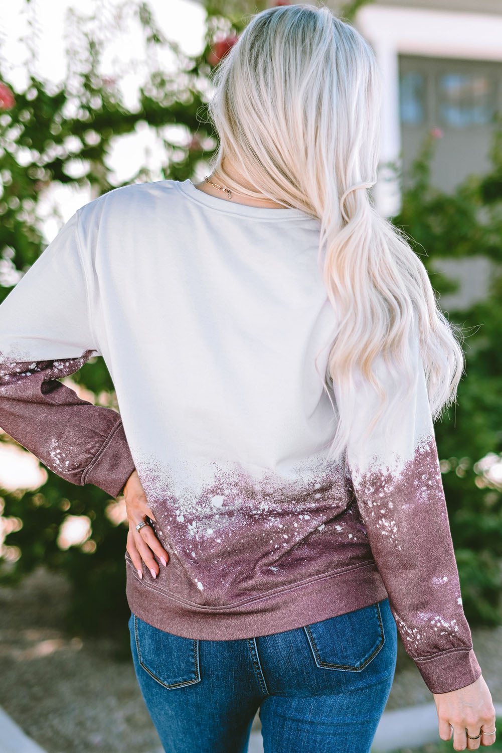 A person with long blonde hair is standing outdoors, facing away from the camera, wearing a Tie Dye Gradient Pullover Sweatshirt featuring a white and brown ombre splatter design.