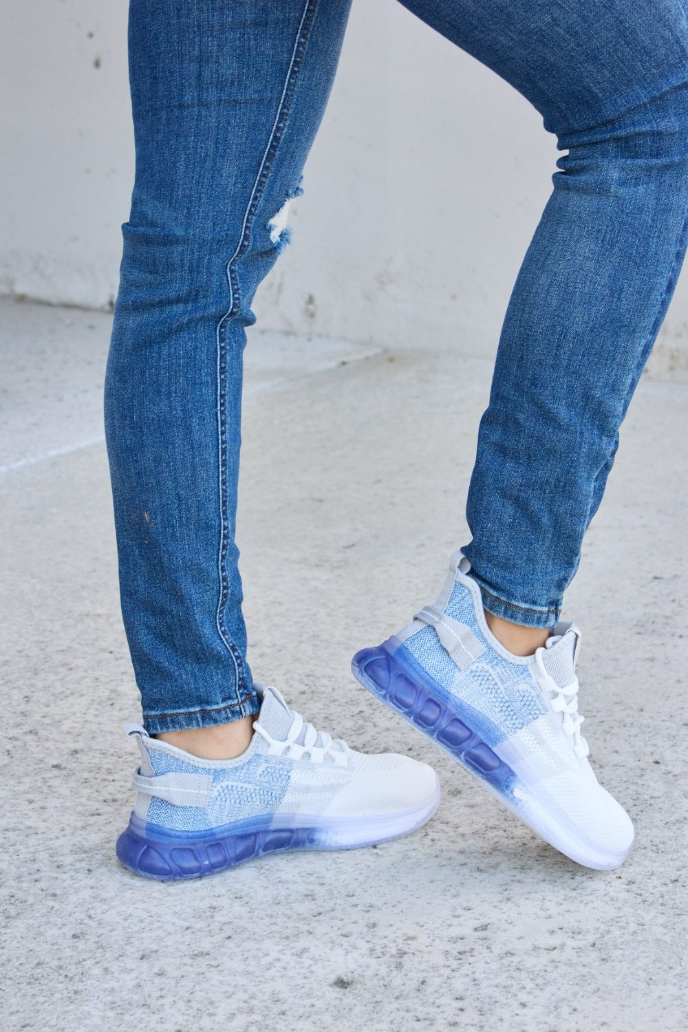 A person wearing distressed blue jeans and a pair of Forever Link Gradient Lace-Up Mesh Breathable Athletic Shoes, standing on a concrete surface.