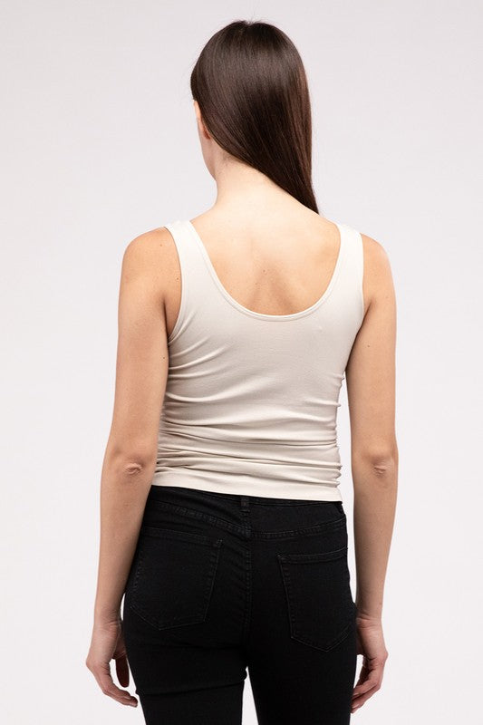 A woman in a white Front & Back 2-Way V-Neck Seamless Tank and black pants, standing with hands on hips and looking at the camera.