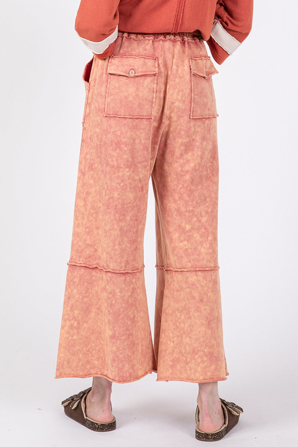 Person wearing SAGE + FIG Mineral Washed Terry Wide Leg Pants with an adjustable waistband and oversized pockets in orange, paired with sandals and a striped top.