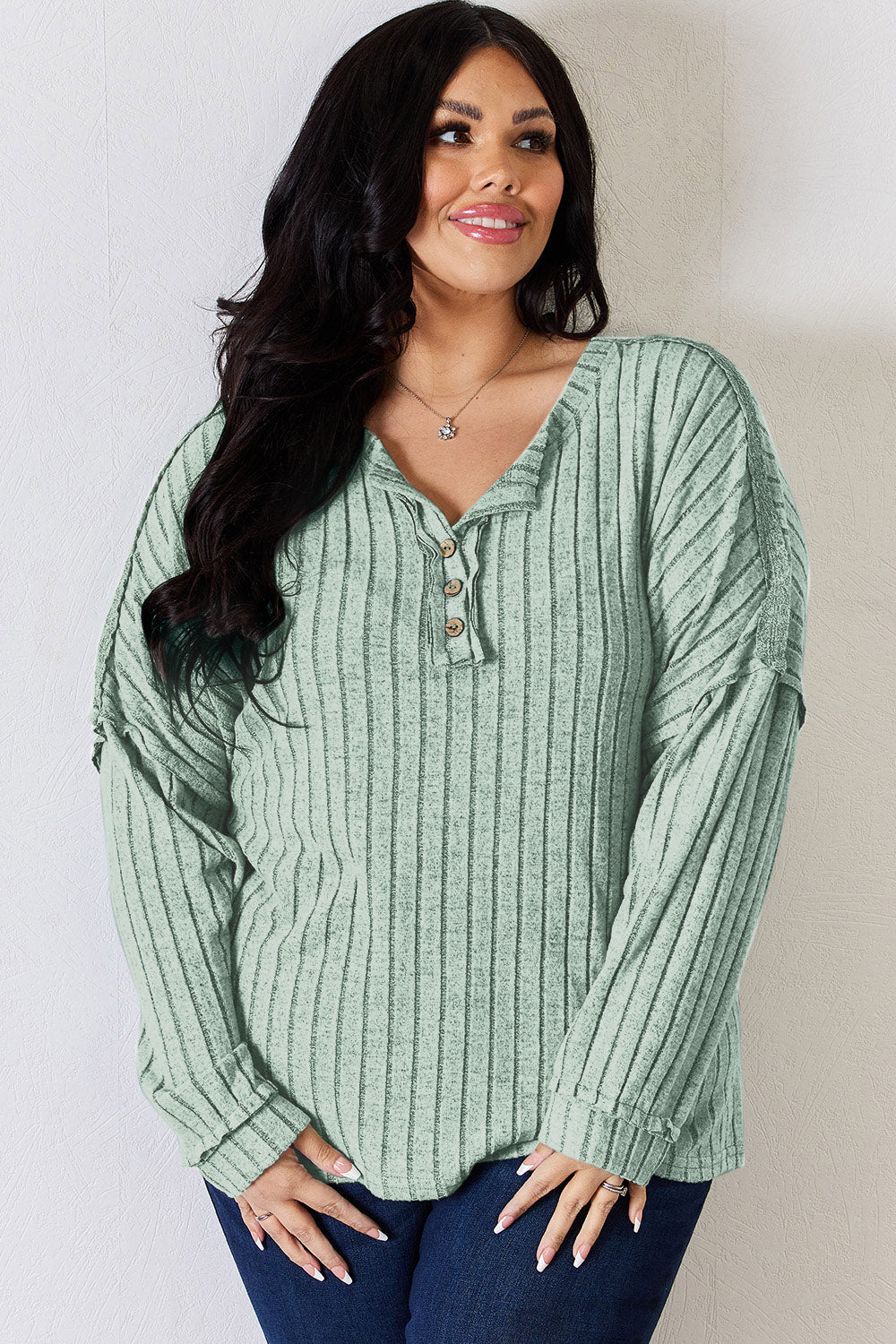 A woman with long, wavy blonde hair wears a slightly stretchy, textured Basic Bae Full Size Ribbed Half Button Long Sleeve T-Shirt in pink, standing against a neutral backdrop.