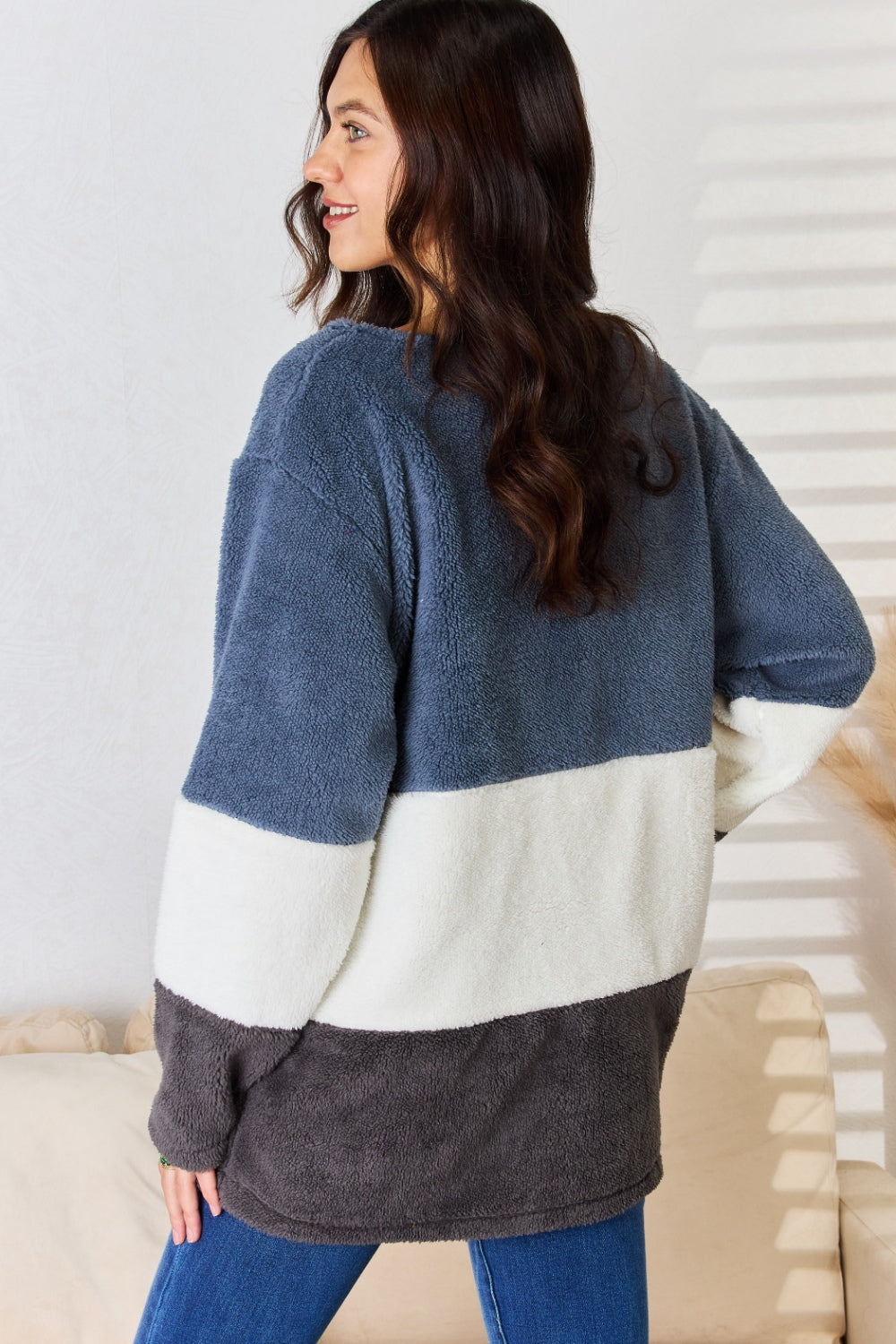 A woman with long, dark hair smiles while wearing the Culture Code Faux Fur Color Block V-Neck Sweater in shades of navy, white, and gray, paired with blue jeans—a versatile wardrobe addition.