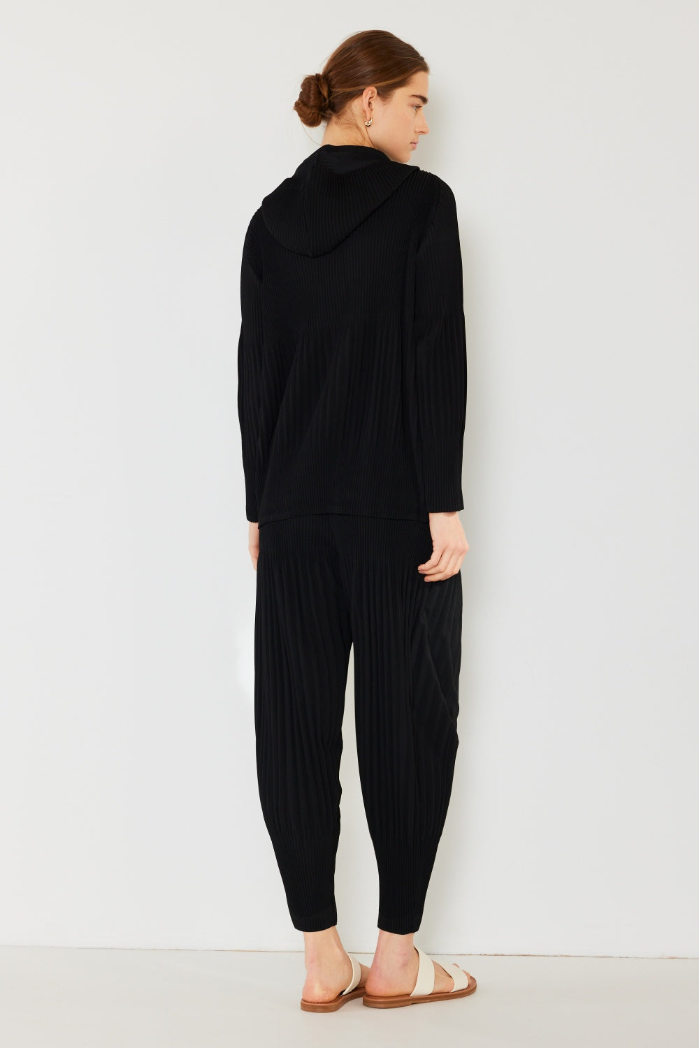 A person stands against a plain background, wearing a matching dark green hooded top and Marina West Swim Pleated Unisex Aladdin Plisse Pants with a ribbed texture, complemented by white sandals.