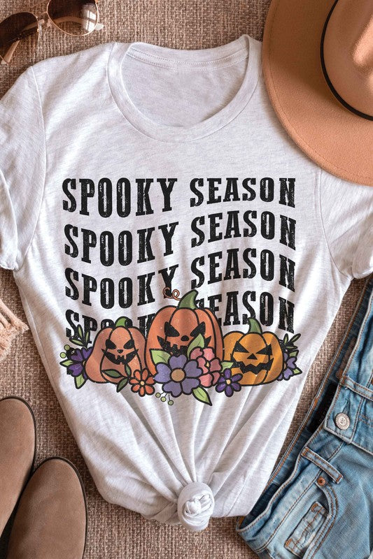 A person is wearing the SPOOKY SEASON PUMPKINS Graphic Tee, featuring "Spooky Season" text and pumpkin graphics, standing with hands by their sides. The unisex sizing ensures a comfortable fit for everyone.