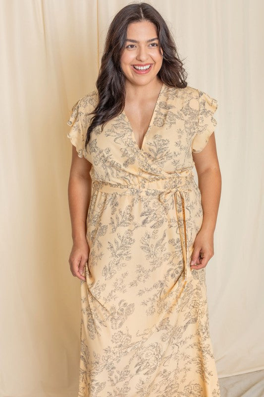 A woman wearing a Floral Surplice Sash Sundress, which is light yellow and unlined, stands smiling against a cream-colored background.