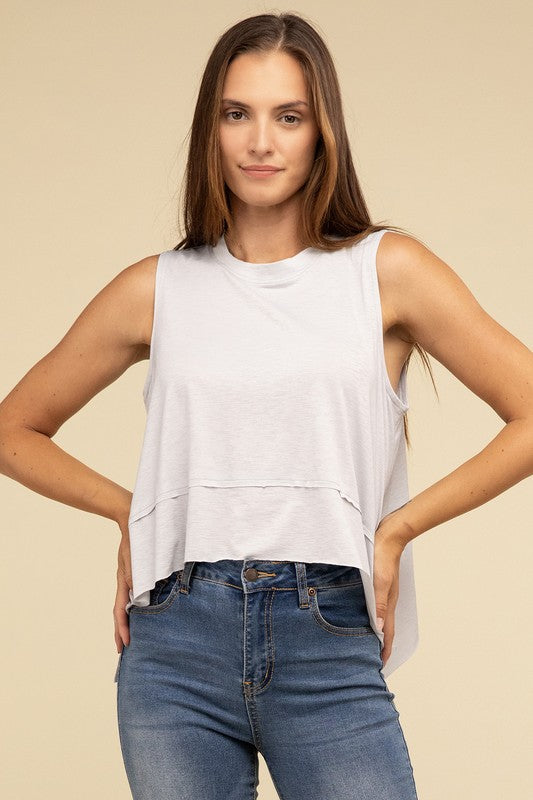 Wearing the Shark Bite Side Slit Short Sleeveless Top in maroon paired with white pants, a model is set against a beige background, exemplifying an effortlessly chic and casual wardrobe.