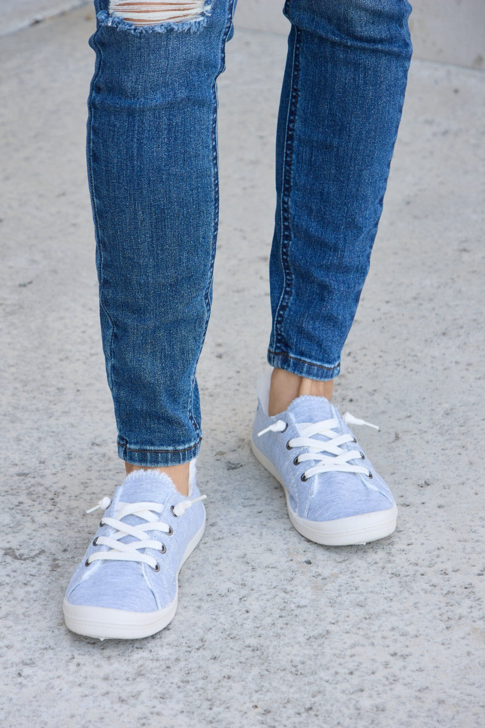 Person wearing ripped blue jeans and Forever Link Lace-Up Plush Thermal Flat Sneakers in grey with white laces, standing on a concrete surface.