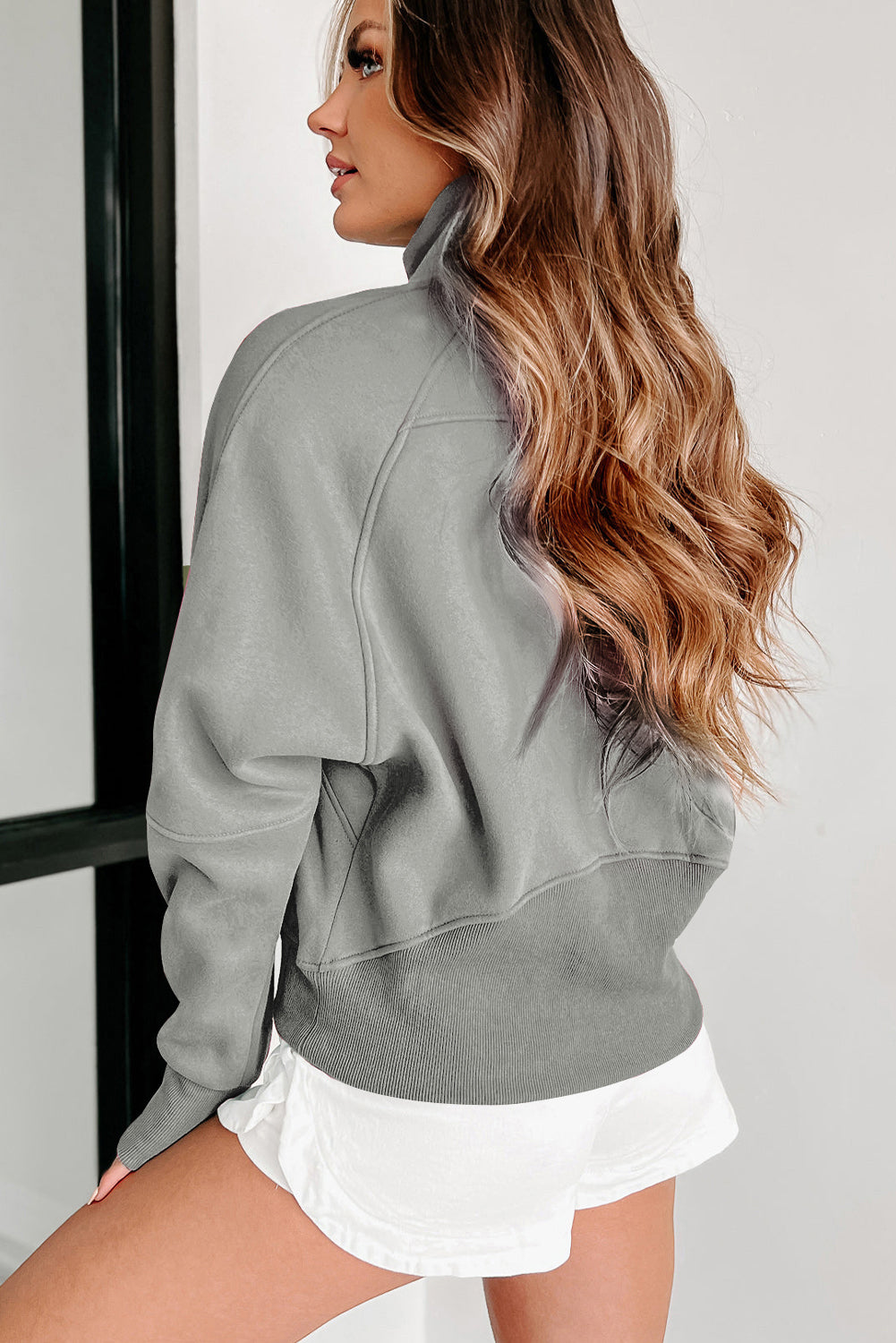 A person with long, wavy hair is seen from behind, wearing a chic Gray Fleece Lined Zip Up Stand Collar Thumbhole Sleeve Sweatshirt and white shorts, perfect for casual outings.