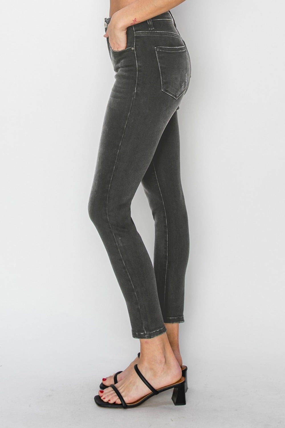 Person wearing RISEN Full Size High Rise Ankle Skinny Jeans and black open-toe heels stands against a plain background.