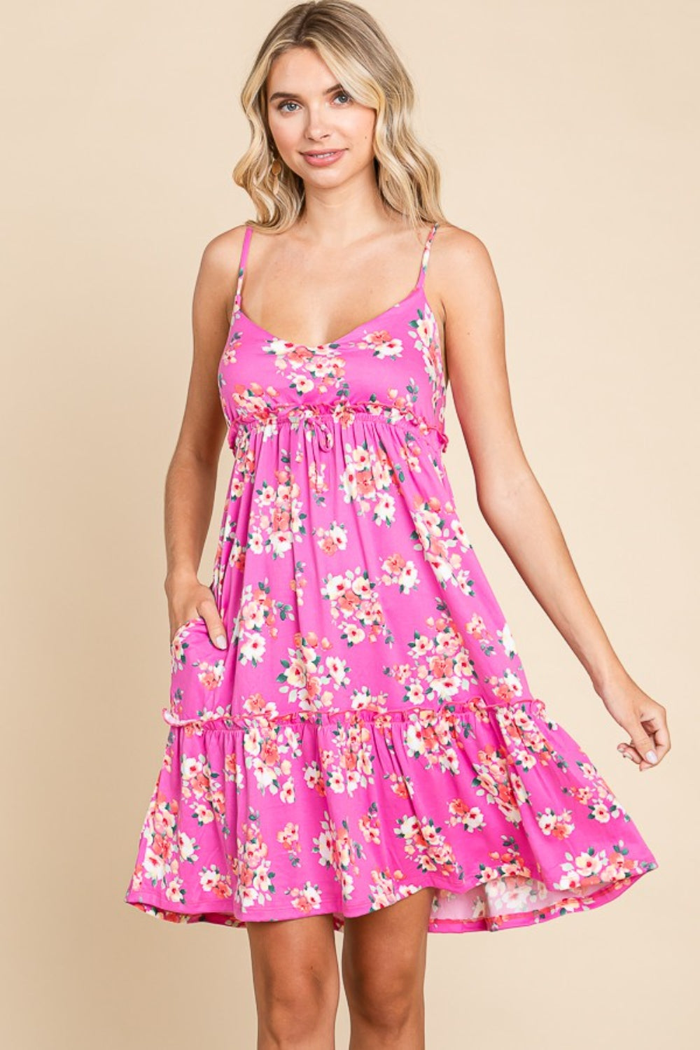 Person wearing a Culture Code Full Size Floral Ruffled Cami Dress with thin straps and a ruffled hem, standing against a beige background. This versatile option exudes feminine charm with its pink, floral design.