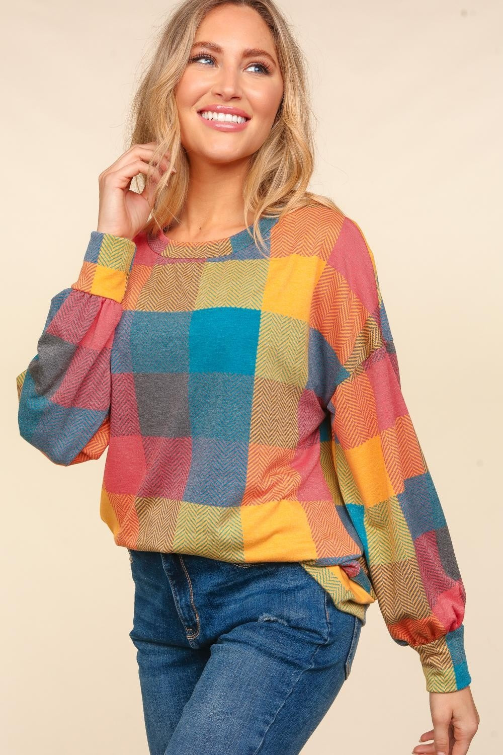 A woman wearing a stylish Haptics Round Neck Color Block Plaid Top and blue jeans poses against a beige background.