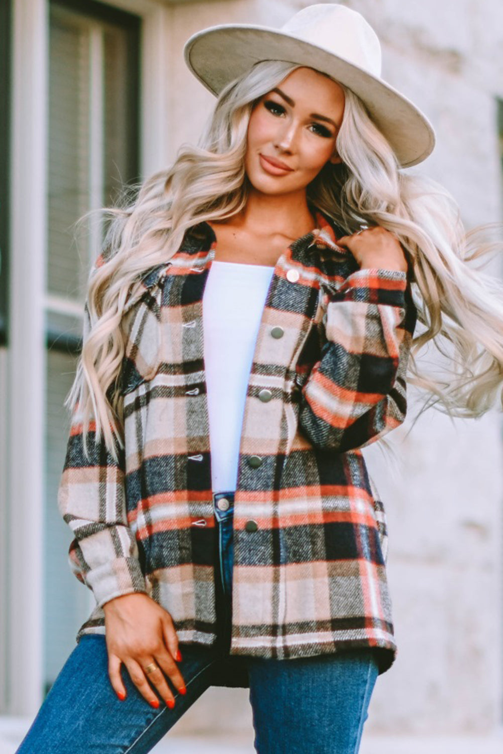 A person wearing a Brown Plaid Button Up Long Sleeve Flannel Shacket layered over a white top with ripped jeans and holding a brown handbag stands against a textured gray wall.