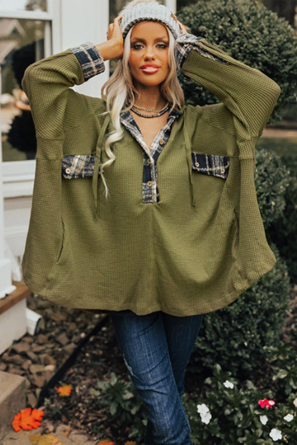 A person wearing a grey beanie, the Green Flowy Plaid Accent Waffle Knit Henley Hoodie, and a plaid shirt is standing outside next to a pumpkin and greenery.