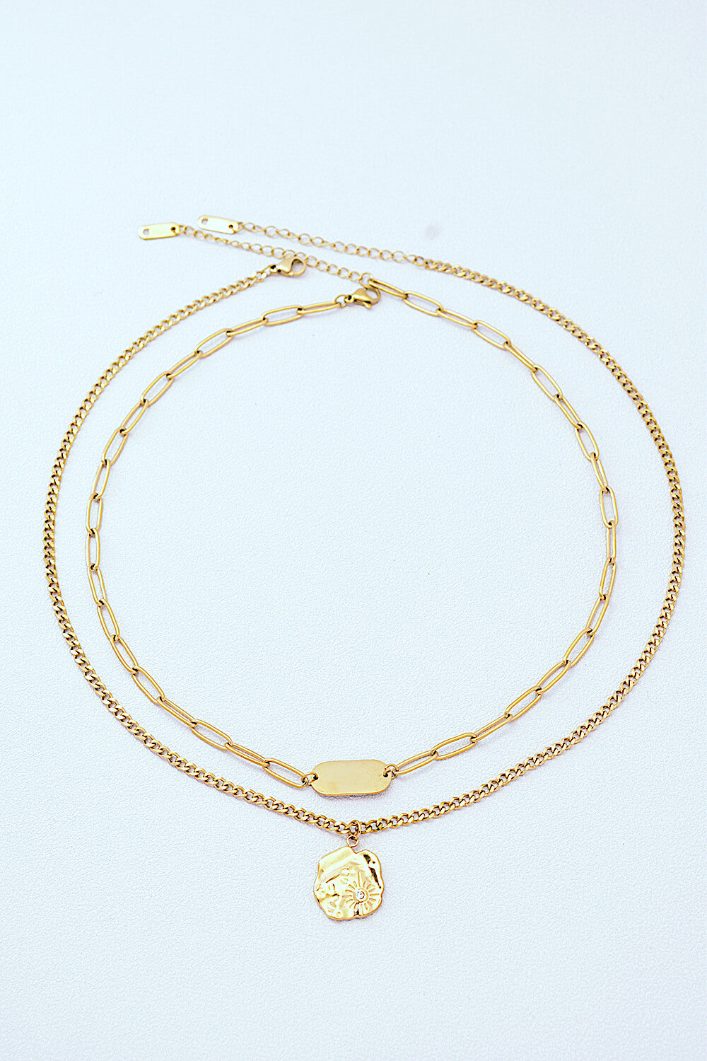 Displayed are two gold necklaces: the Gold-Plated Double-Layered Pendant Necklace featuring a chain link motif, and another necklace boasting a finer chain highlighted by a medallion charm.