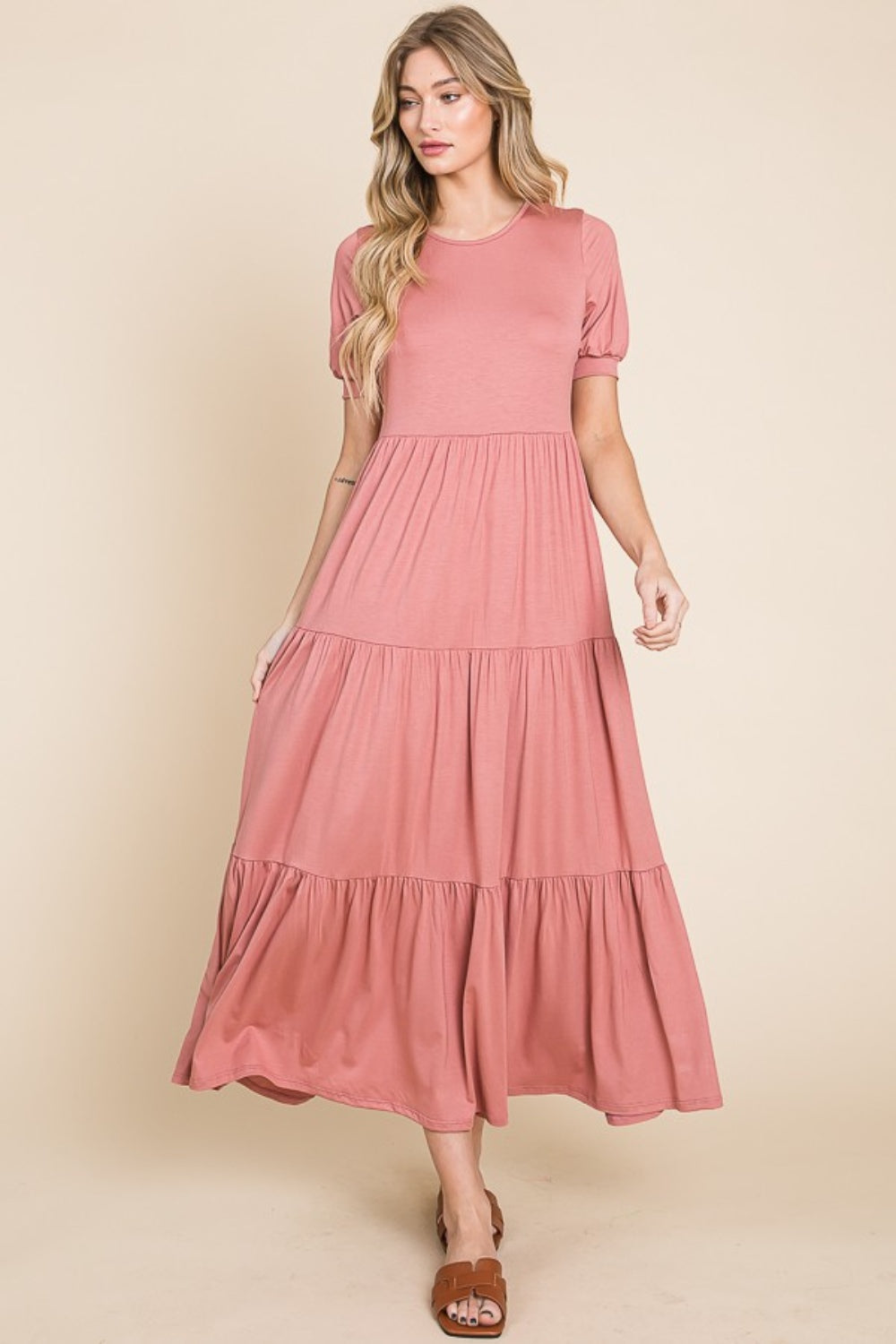 A person wearing the BOMBOM Short Sleeve Tiered Maxi Dress in pink, showcasing its comfortable style with a long, tiered design, stands against a beige background.