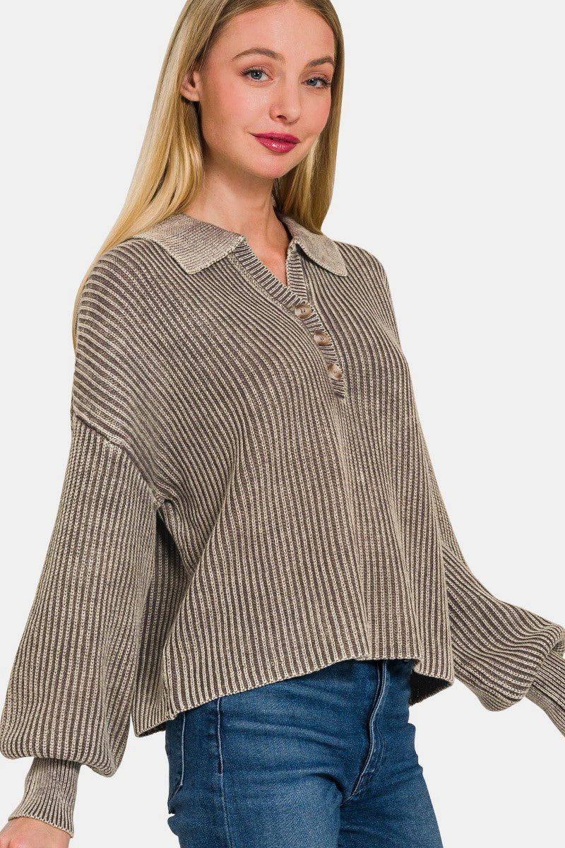 A woman with long blonde hair wearing the Zenana Washed Half Button Long Sleeve Sweater, made of 100% cotton and featuring a striped oversized design, pairs it with jeans as she stands against a plain background, smiling with one hand touching the sweater's collar.