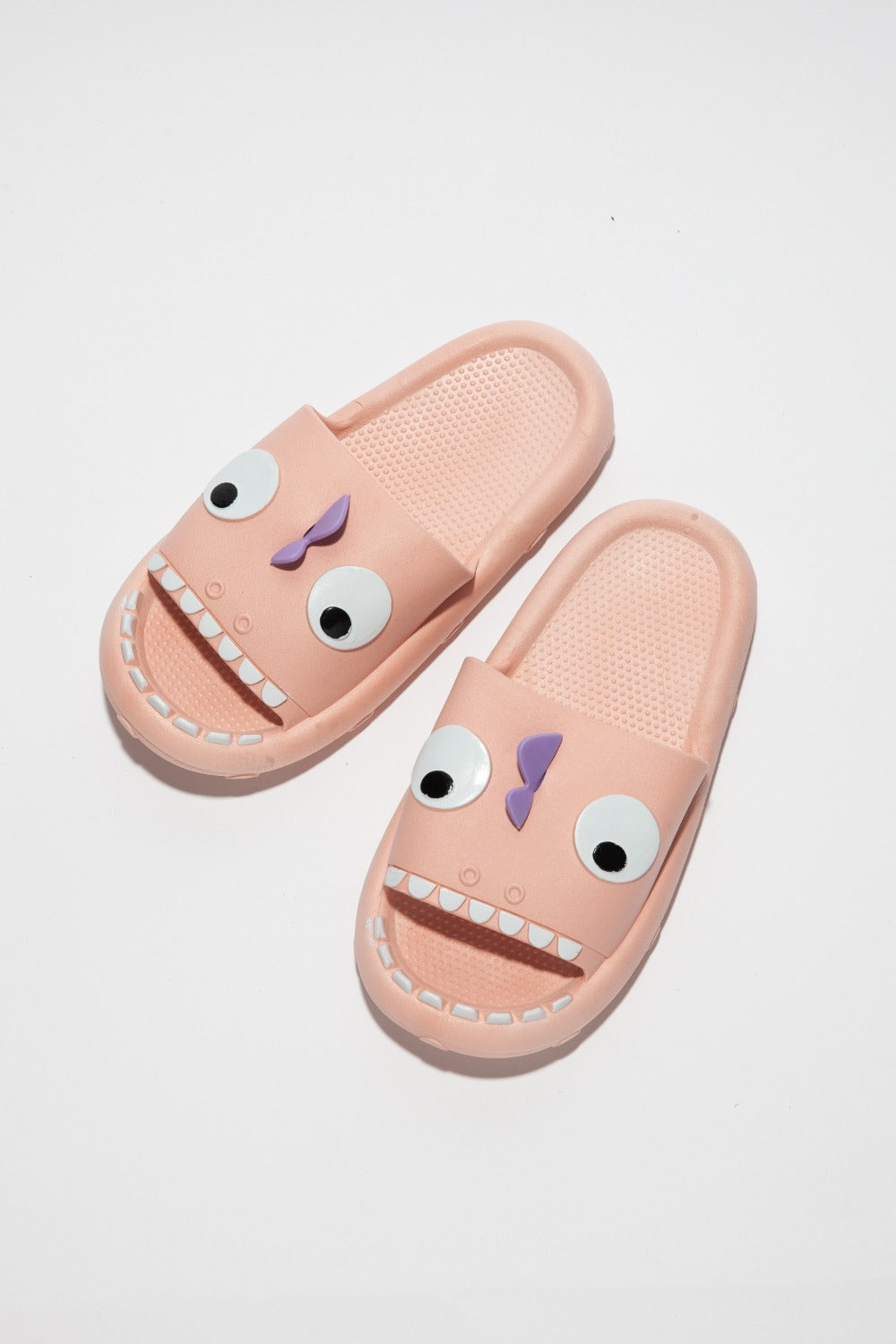 The NOOK JOI Monster Pillow Cloud Slides Non-Slip Slipper features cartoonish monster faces with large eyes, a purple nose, and an open mouth with teeth. Made of durable EVA material, these fun pink cloud slippers also boast an anti-slip design for added safety.