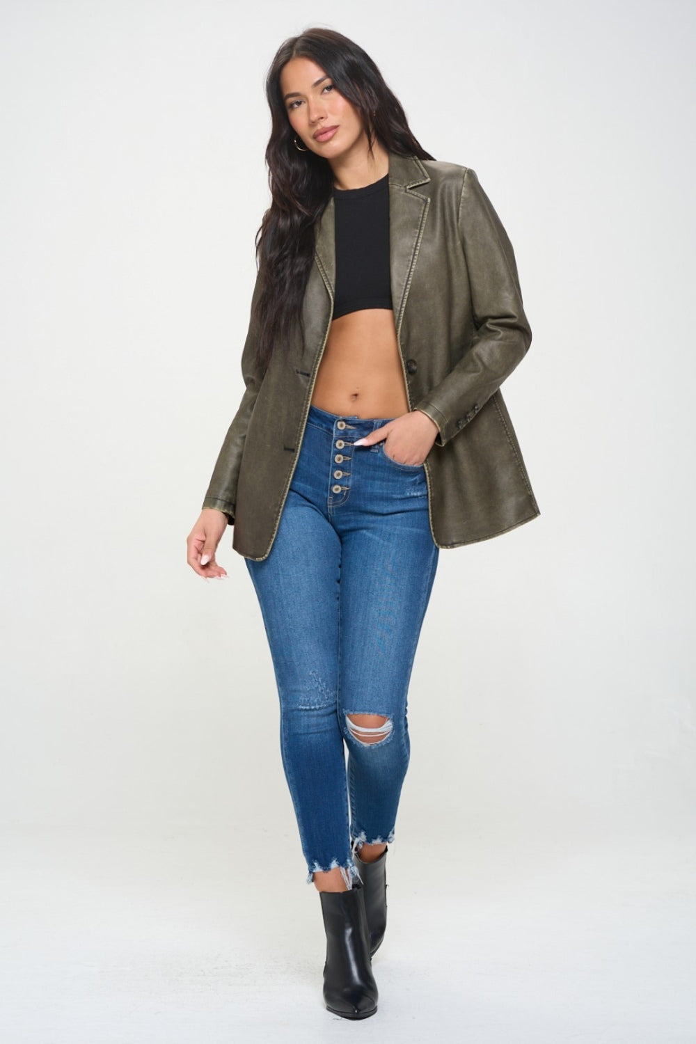 A person with long dark hair wears the Coalition LA Single-Breasted Vegan Leather Blazer in olive green over a black crop top and blue jeans against a neutral background, showcasing a stylish and ethical fashion choice.