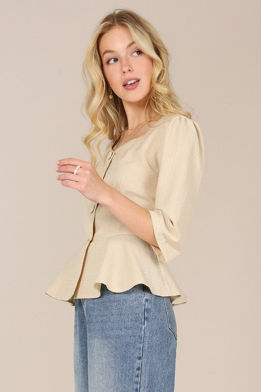 A person with long blonde hair is posed against a plain background, wearing a beige 3/4 sleeve front button blouse paired with puff sleeves and blue jeans.