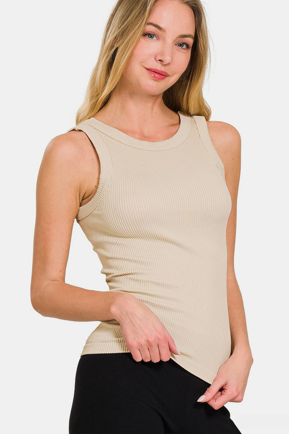 A person with long hair wears the Zenana 2 Way Neckline Washed Ribbed Tank—a beige, essential versatile wardrobe piece—paired with black pants, smiling slightly against a plain white background.