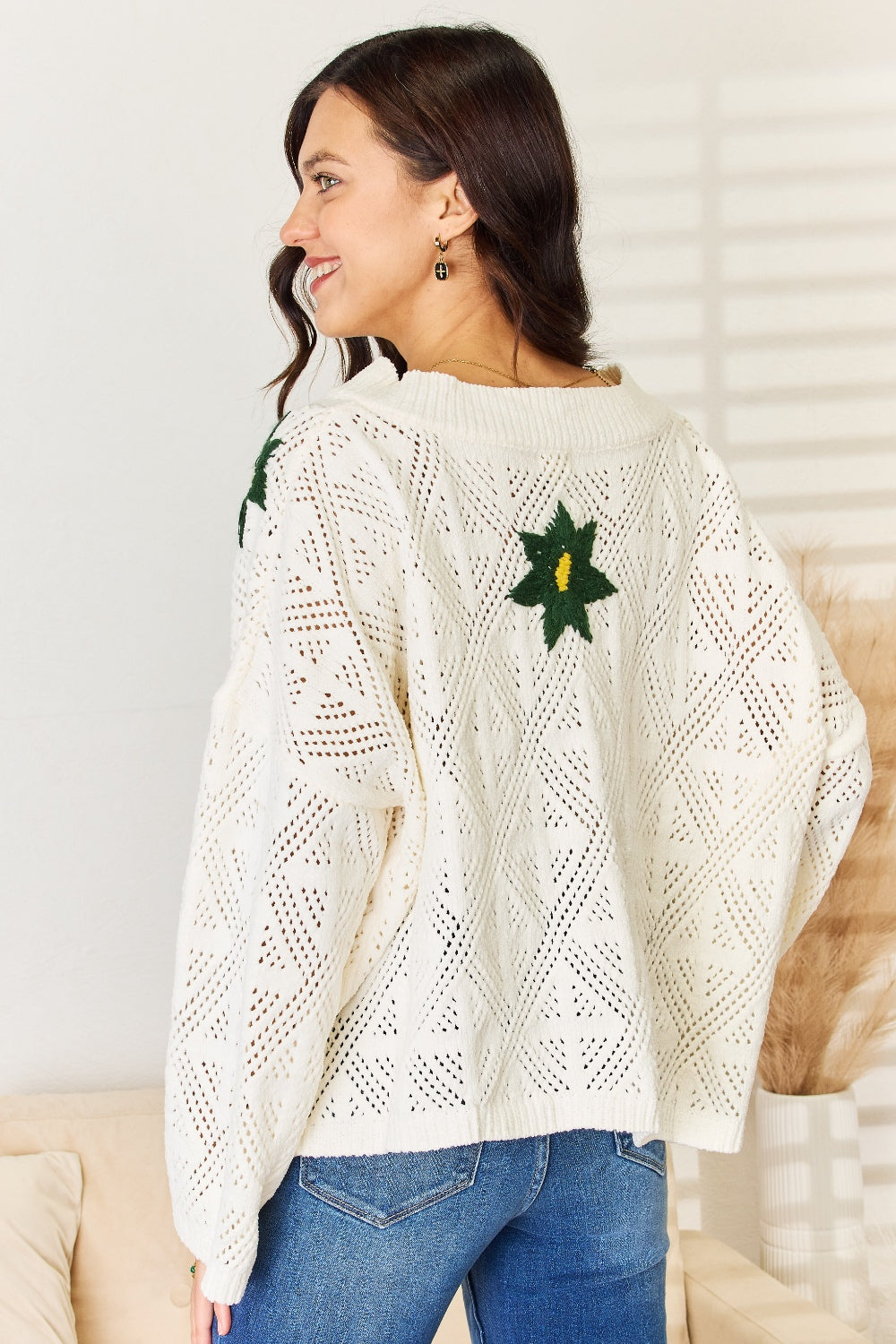 A woman wearing the POL Floral Embroidered Pattern V-Neck Sweater in creamy chenille paired with blue jeans, standing indoors.