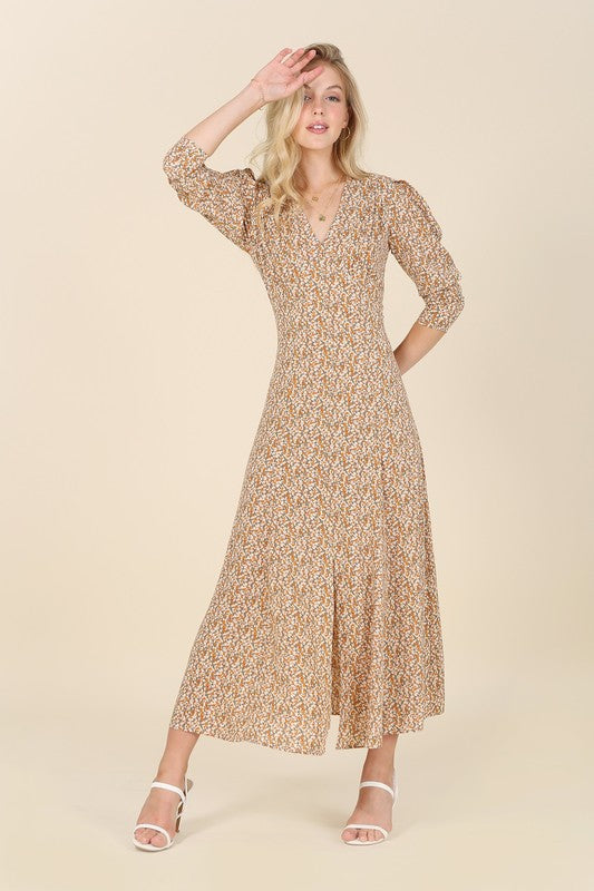 A woman gracefully poses against a beige background wearing the Fit and Flare floral maxi dress, featuring a V-neckline, elegant puff sleeves, and a complementary front slit.