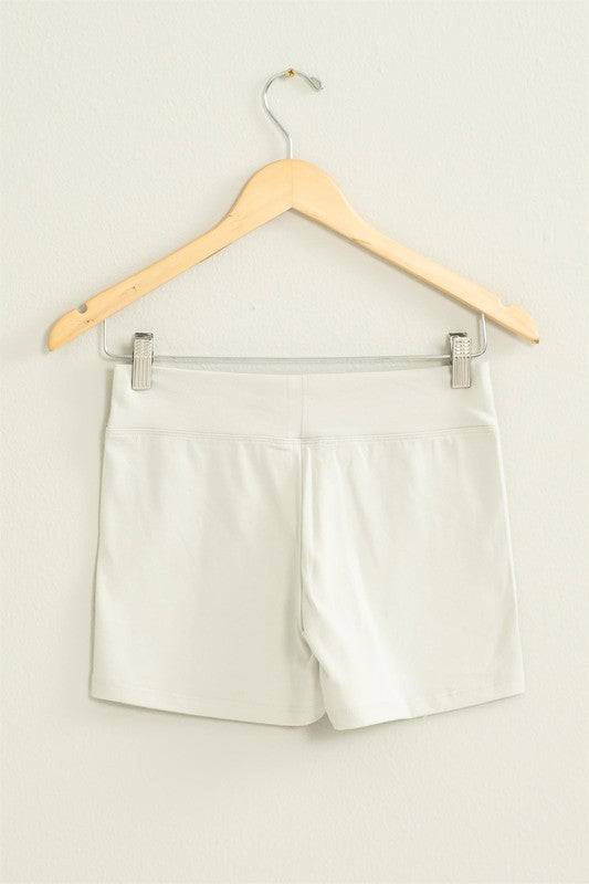 The Take Pride Mid-Rise Biker Shorts, crafted from stretch fabric, hang gracefully on a wooden hanger against a pale wall.