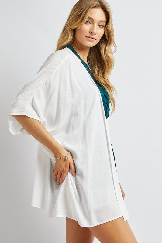 A woman poses against a simple backdrop, gracefully wearing a wardrobe essential: the Favorite Solid Kimono Cardigan in pink. Complementing her white tank top and denim shorts, this casual layer enhances her relaxed style with an elegant touch.