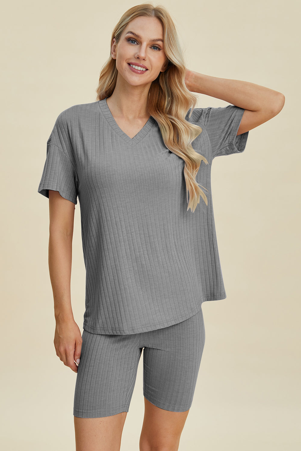 A woman with long blonde hair wearing the Basic Bae Full Size Ribbed V-Neck Short Sleeve Top and Shorts Set in rust stands against a plain background. This stylish two-piece set is made from a comfortable, stretchy fabric that is also machine washable.