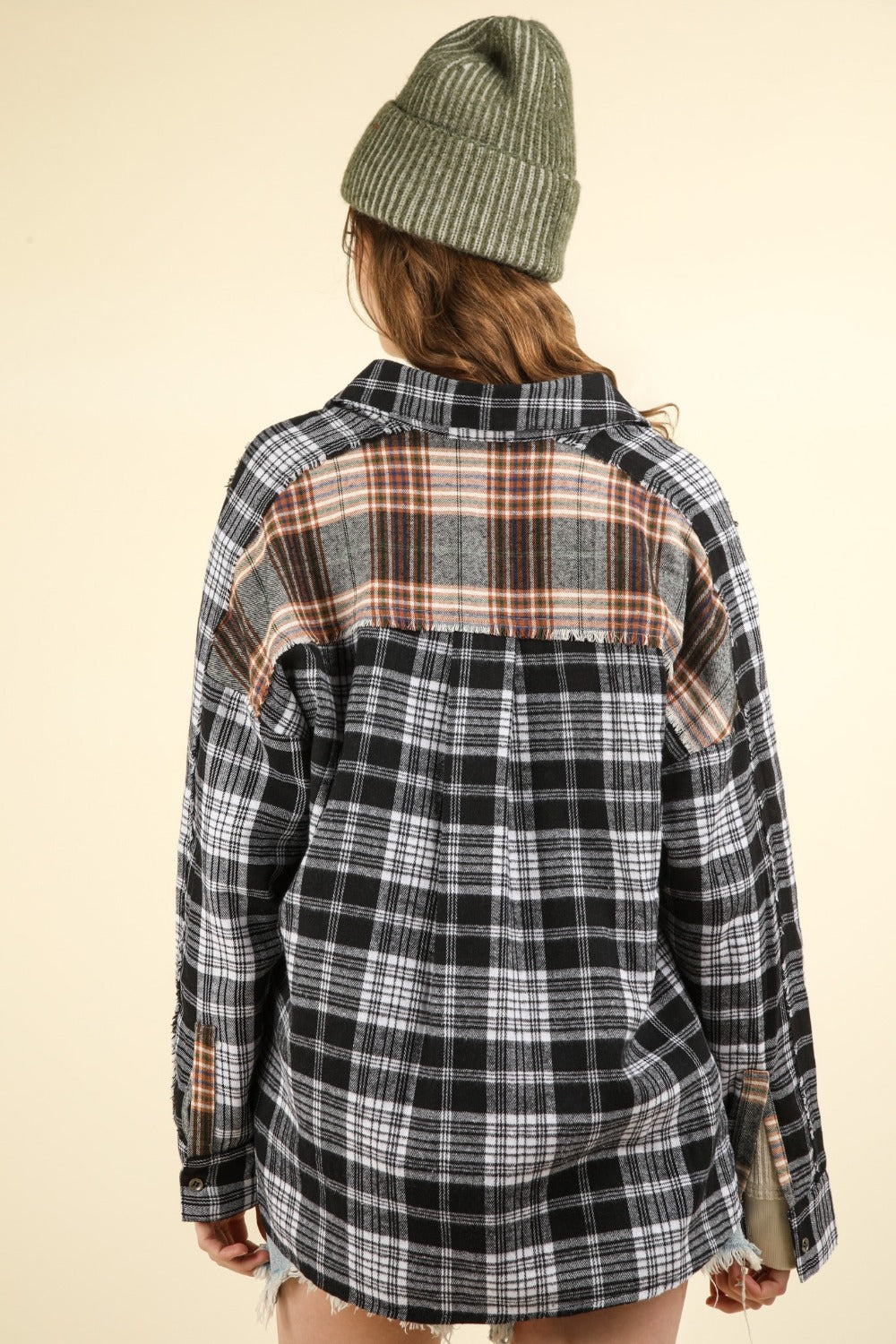 A person wearing an oversized VERY J Contrast Plaid Raw Detail Shirt, a beige beanie, and denim shorts stands against a plain background.