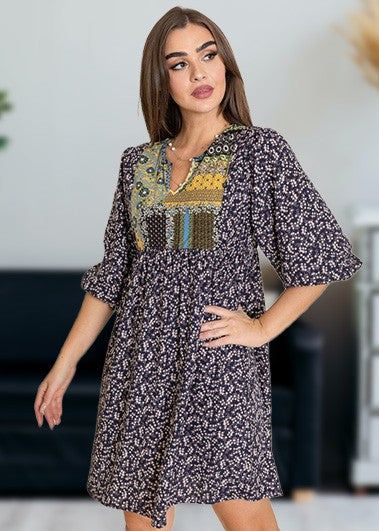 A woman wearing a 3/4 sleeve Ditsy Floral Patch Panel Boho Dress is standing gracefully in a room with a sofa in the background.