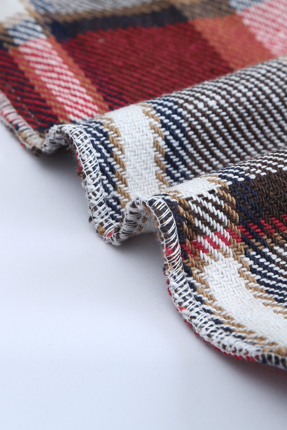 A person wearing a Brown Plaid Button Up Long Sleeve Flannel Shacket layered over a white top with ripped jeans and holding a brown handbag stands against a textured gray wall.