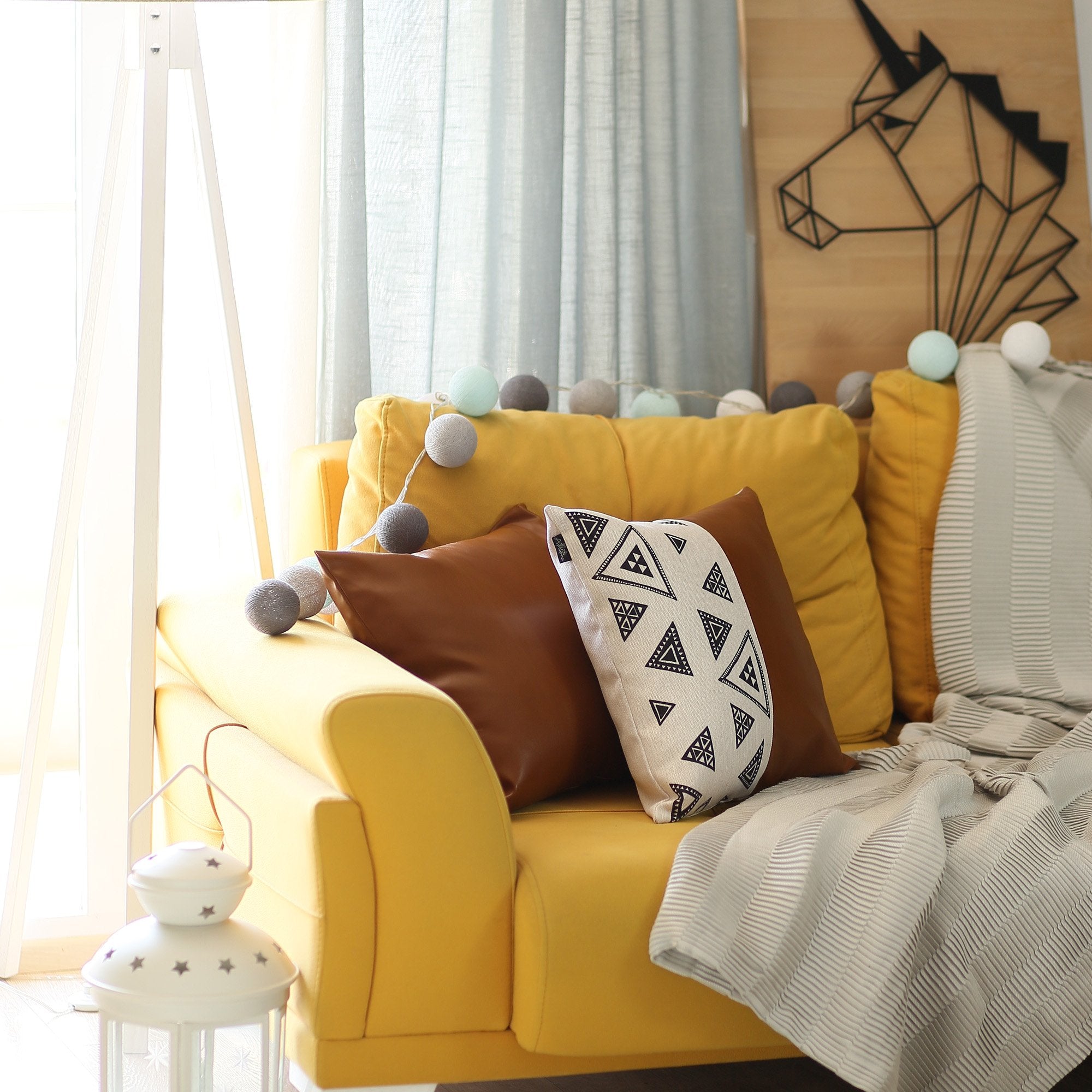 Resting on a yellow cushion is the Bohemian Handmade Decorative Single Throw Pillow, featuring vegan faux leather with a geometric pattern on one half. The setup is completed with round lights draped over it, showcasing the eclectic charm of bohemian throw pillows.