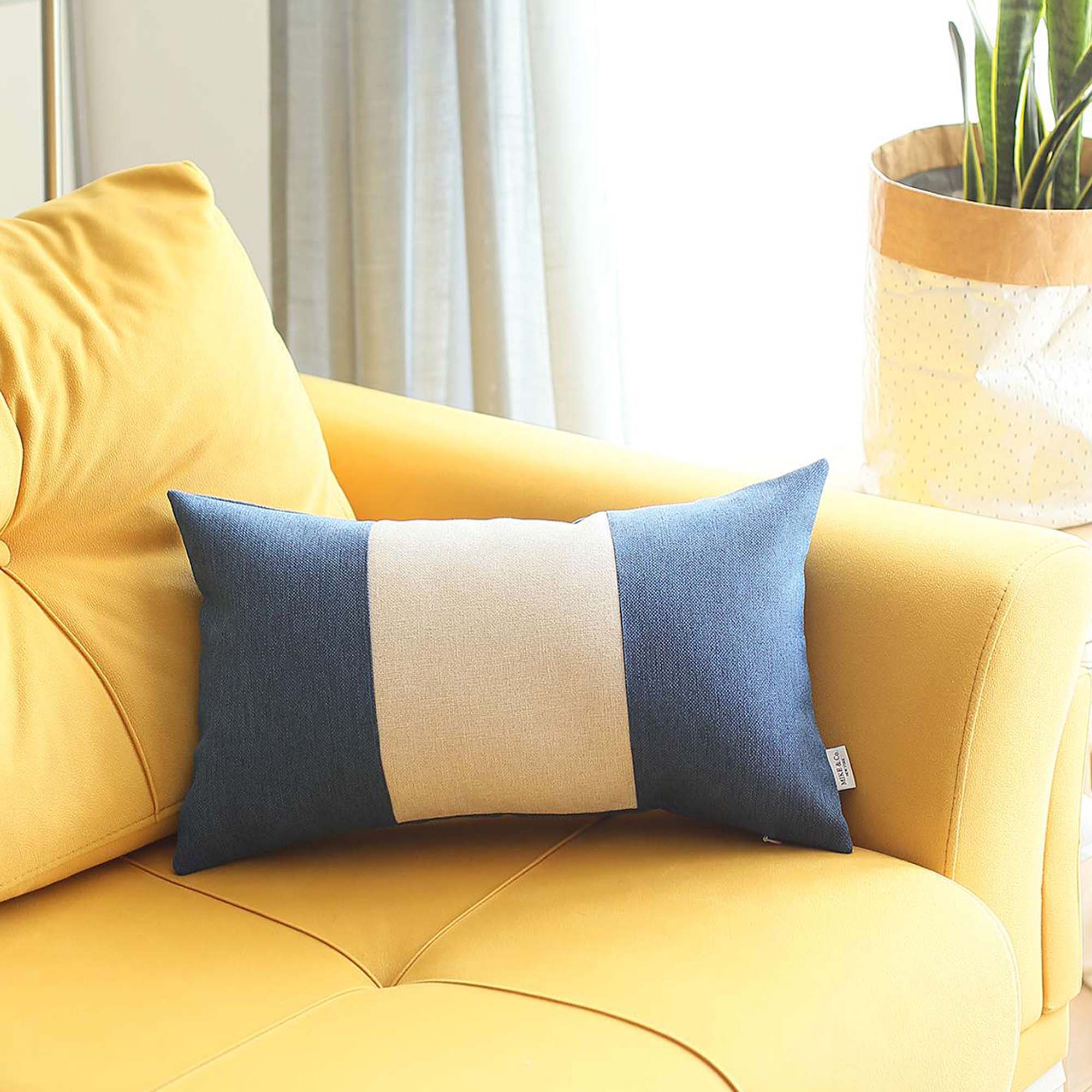 A Bohemian Handmade Decorative Throw Pillow in solid Jacquard, featuring black, gray, and yellow stripes, rests on a brown sofa beside a wooden shelf holding a rolled-up magazine.