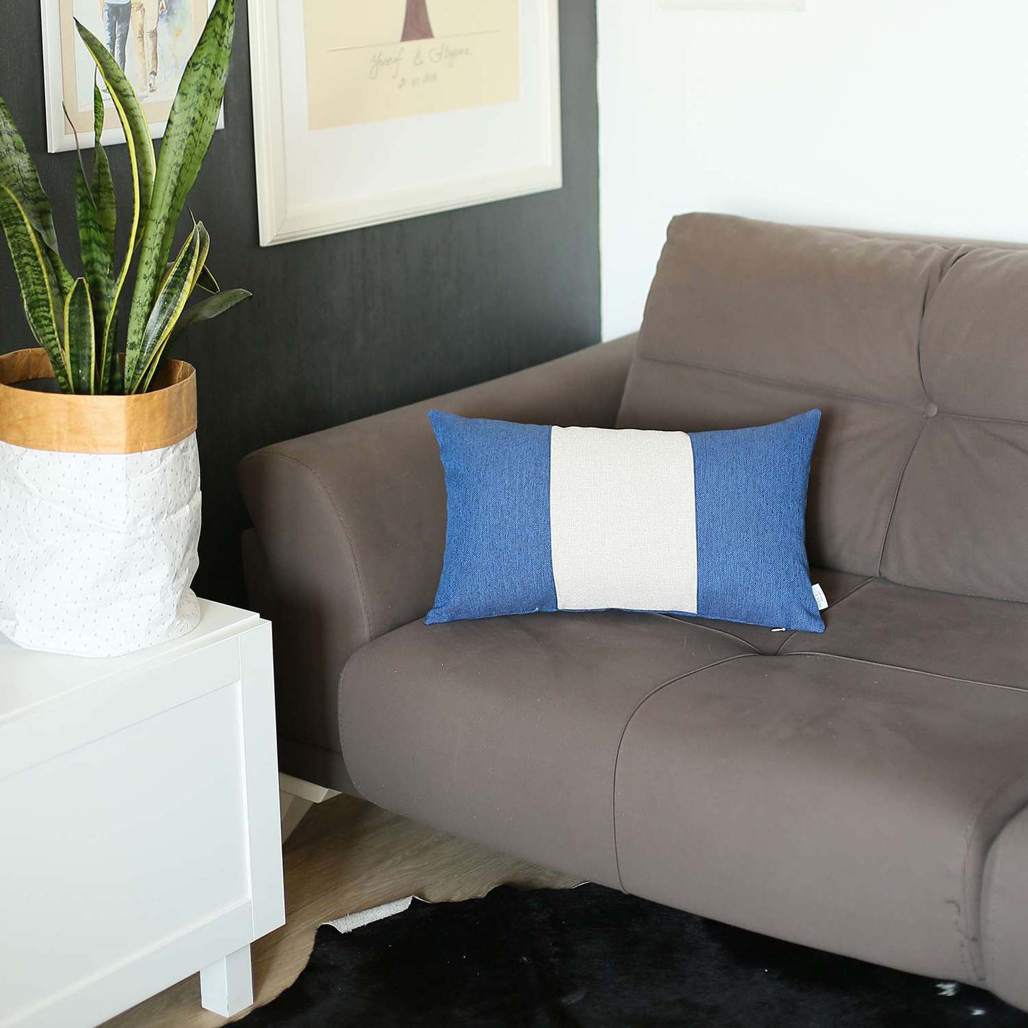 A Bohemian Handmade Decorative Throw Pillow in solid Jacquard, featuring black, gray, and yellow stripes, rests on a brown sofa beside a wooden shelf holding a rolled-up magazine.