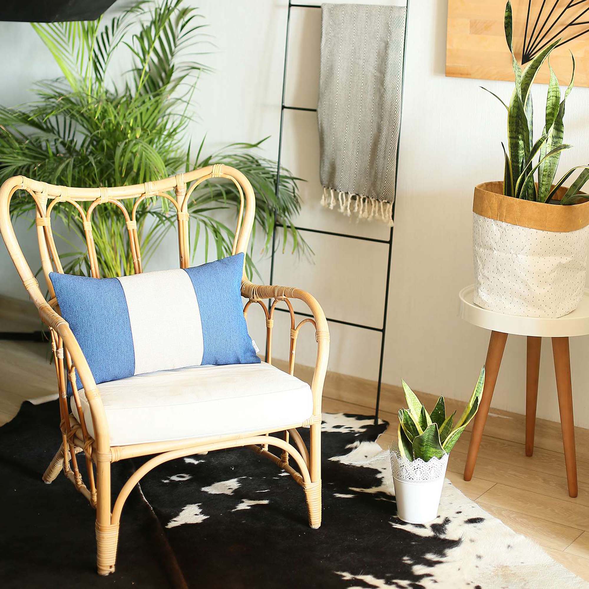 A Bohemian Handmade Decorative Throw Pillow in solid Jacquard, featuring black, gray, and yellow stripes, rests on a brown sofa beside a wooden shelf holding a rolled-up magazine.