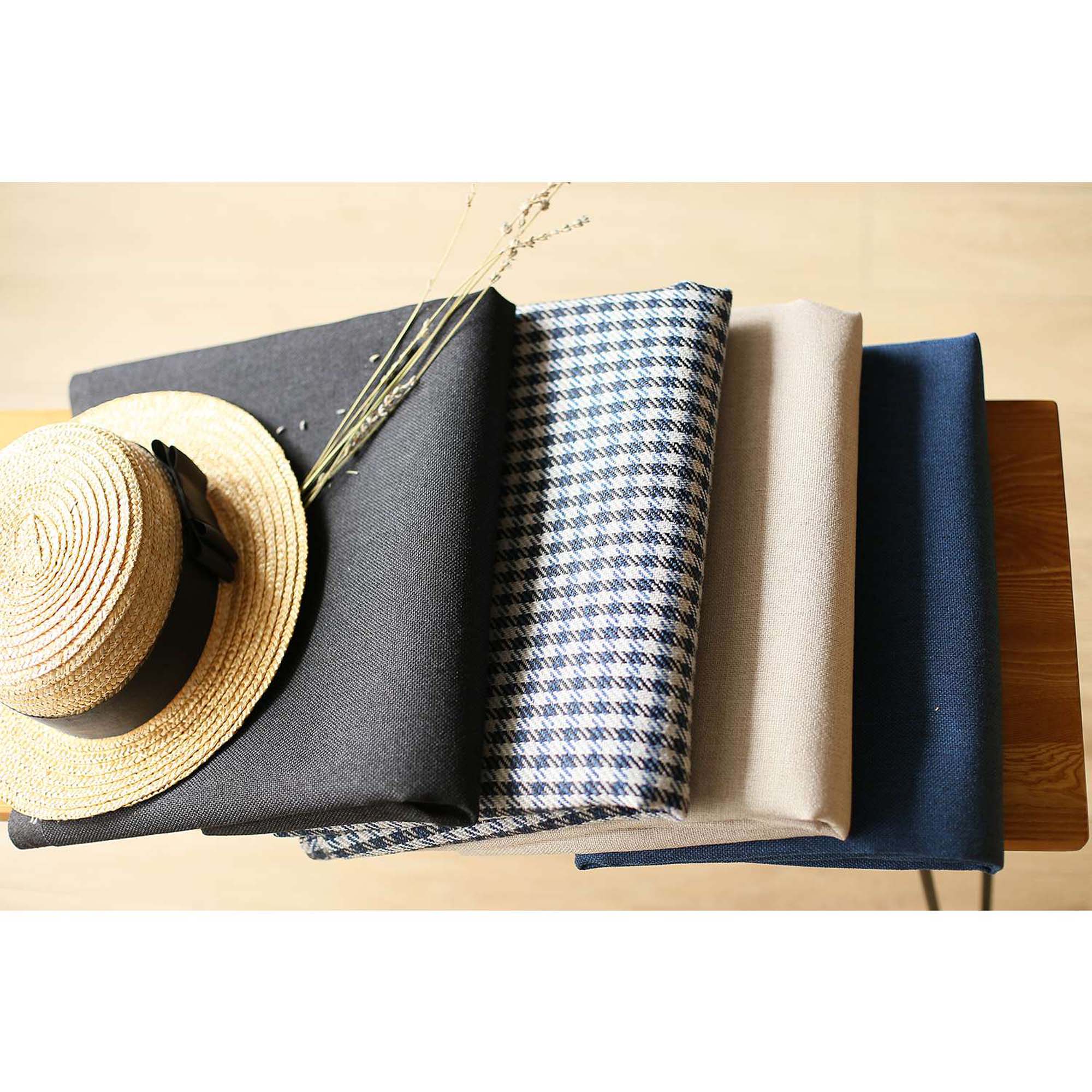 A Bohemian Handmade Decorative Throw Pillow in solid Jacquard, featuring black, gray, and yellow stripes, rests on a brown sofa beside a wooden shelf holding a rolled-up magazine.