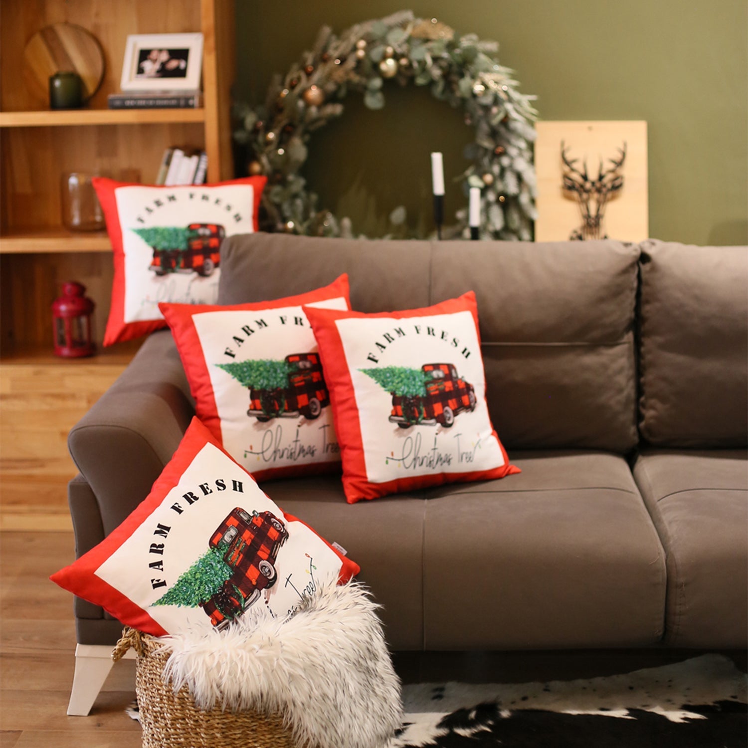 The Christmas Truck Decorative Throw Pillow Set of 4, each measuring 18" x 18" in festive red and white, features a charming design of a red truck carrying a Christmas tree with the "Farm Fresh" text. These pillows are perfect for adding holiday warmth to your sofa or bedding. The cozy setup is enhanced by a basket and fur blanket on the floor, while other festive decor brightens the background. Conveniently machine washable pillow inserts make this an ideal choice for your holiday decor.