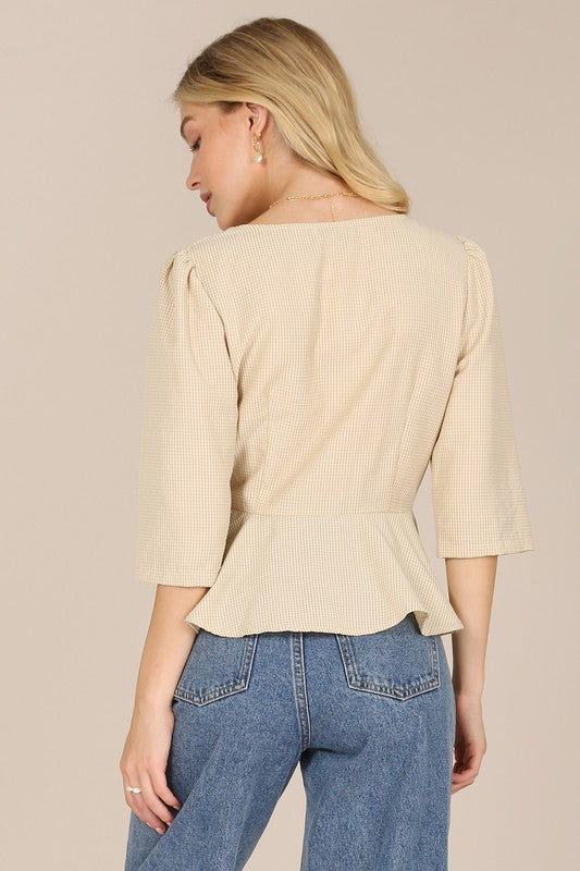 A person with long blonde hair is posed against a plain background, wearing a beige 3/4 sleeve front button blouse paired with puff sleeves and blue jeans.