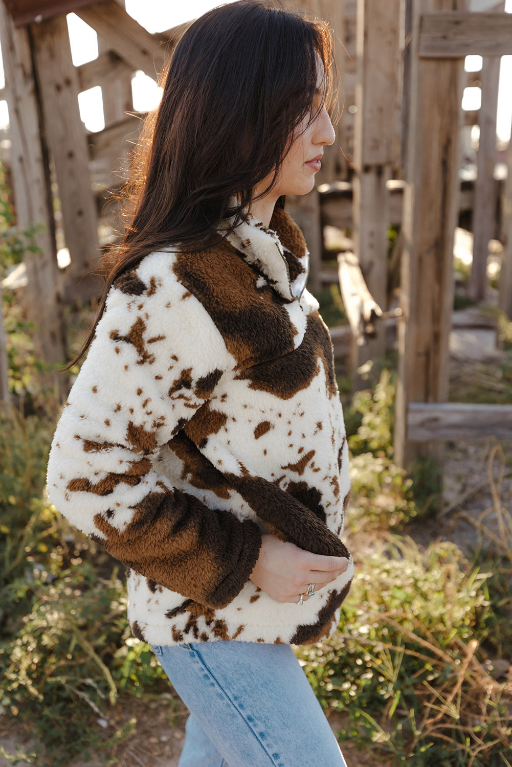 A person wearing a Zip Collar Cow Print Fleece Sweatshirt and light blue jeans stands outdoors with their back to the camera, showcasing the skin-friendly fleece material.