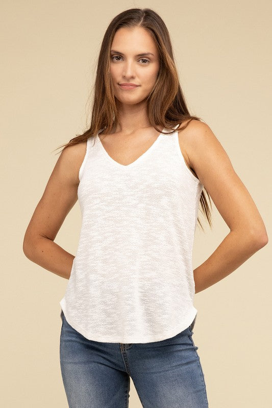 A woman in a stylish and adaptable V Neck Sleeveless Cami Top paired with jeans stands against a beige background. She has long brown hair and maintains a neutral expression.